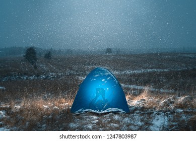 A tourist lies in a tent and reads a book before bedtime. Outside it's the first snow. Winter came