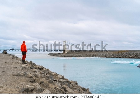 Tourist looking to icebergs in Jokulsarlon glacier lagoon near bridge. Lake in Vatnajokull Nalional park Iceland. Popular attraction. 