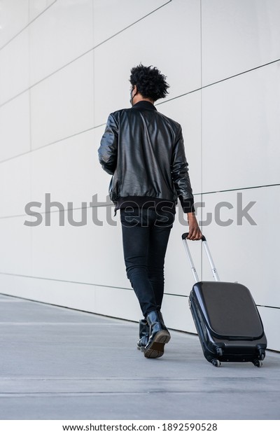 Tourist man\
carrying suitcase while walking\
outdoors.