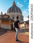 Tourist man with detailed close up view on Michelangelos Dome of St Peter Basilica in Vatican City, Rome, Lazio, Europe, EU. Architectural masterpiece of Papal Basilica of Saint Peter on sunny day