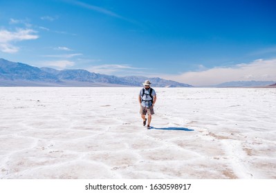 A tourist man with a hat to curb from the sun and a traveler's backpack enjoys a sunny day in the Death Valley desert - Shutterstock ID 1630598917