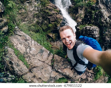 tourist man on a waterfall background holds an action camera and takes a picture of Selfie.