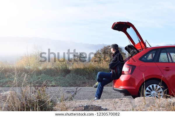 Tourist man sitting on backside red car \
enjoy with view of mountain morining\
light