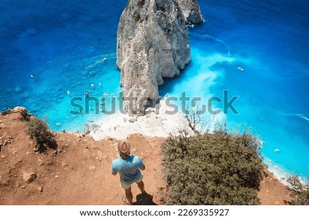 A tourist man stands carefully at the viewpoint of Keri and enjoys the view of the famous Mizithres rocks with turquoise sea at Zakynthos island, Greece
