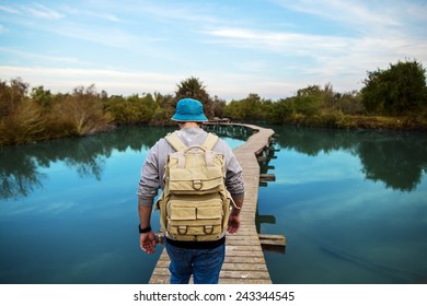 tourist man walking across wooden bridge over glossy blue lake