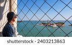 Tourist man wearing hat with aerial view from St Mark bell tower Campanile of old town Venice, Veneto, Italy, Europe. Looking at San Giorgio Maggiore island, Venetian lagoon. UNESCO World Heritage