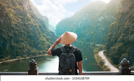 Tourist man is wearing Non La (Vietnamese tradition hat) with backpack and enjoy sightseeing at beautiful landscape in Ninh Binh (Vietnam)