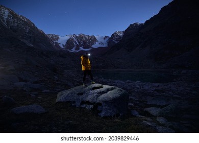 Tourist Man In Yellow Jacket With Headlamp In The Snow Mountains Under Night Sky With Stars.