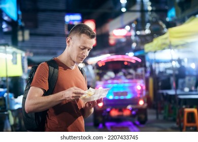 Tourist In Night Bangkok. Man With Backpack Eating Local Food At Street Market. 
