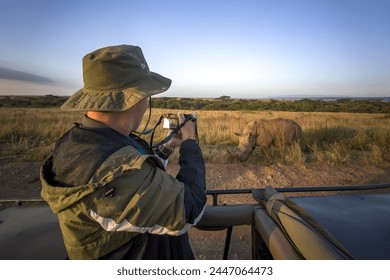 A tourist photographs a wild leopard during a safari tour in Kenya and Tanzania. Concept Travel and adventure through wild Africa. A man with a camera in an open-top safari car is traveling in Africa.