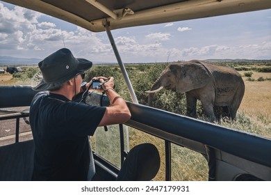 A tourist photographs a wild leopard during a safari tour in Kenya and Tanzania. Concept Travel and adventure through wild Africa. A man with a camera in an open-top safari car is traveling in Africa. - Powered by Shutterstock