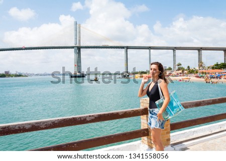Tourist posing for photos in Redinha beach (Natal / Brazil) with Newton Navarro Bridge in background.
