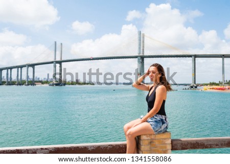 Tourist posing for photos in Redinha beach (Natal / Brazil) with Newton Navarro Bridge in background.