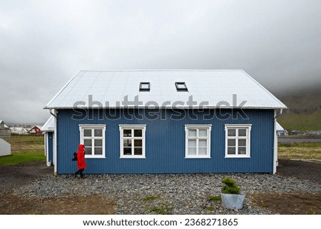 A tourist in a red coat walks near a blue wooden house in Seydisfjörður village, Iceland, Scandinavia, Europe