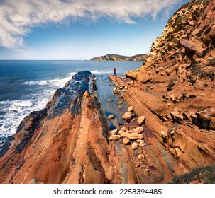 Tourist in red jacet stands on the end of cape in Dalan and Voge hiking area. Colorful seascape of Adriatic sea. Sunny morning scene of Albania, Europe. Beauty of nature concept background.