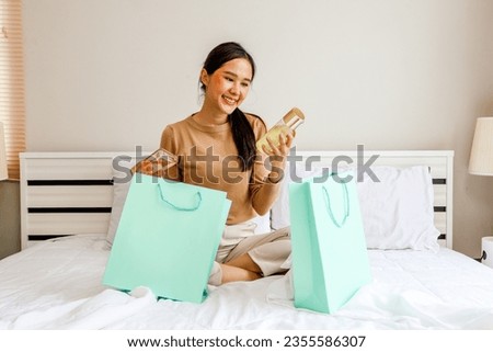Tourist shopper beautiful asian woman sitting and relaxing on hotel bed, happy traveling shopping, cosmetics, french perfume, best selling products duty free with discount promotion in shopping mall.