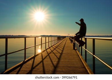 Tourist Sit On Wharf Construction And Enjoy Morning At Sea. Sunny Clear Blue Sky, Smooth Water Level