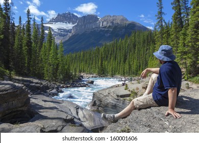 Tourist Sitting On The Brink Of A Canyon And Looking At Far Mountains (Jasper National Park. Alberta. Canada)