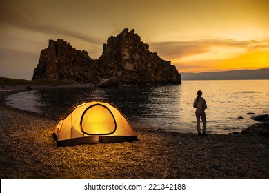 Tourist stand near tent and lake shore and looking at the beautiful sunset - Powered by Shutterstock