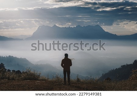 Tourist standing on the edge of the cliff holding flowers looking at the beautiful Doi Luang Chiang Dao mountain in the morning at Chiang Mai , Thailand