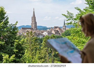 A tourist studies a map while enjoying a stunning view of Freiburg im Breisgau, Germany. The cityscape, cathedral, and greenery make it perfect for travel blogs and European adventures.