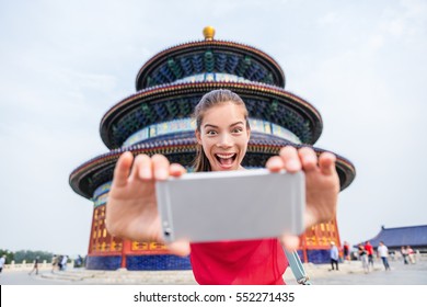 Tourist Taking Goofy Face Funny Selfie On Travel. Happy Young Woman Having Fun With Mobile Phone At Famous Beijing Landmark. Temple Of Heaven China Travel.