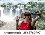 Tourist taking a photo in front of the Iguazu Falls, Argentina. Happy tourist taking a selfie at Iguazu Falls. Tourist with hat taking a selfie in front of imposing landscape