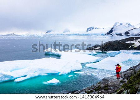 Tourist taking photos of amazing frozen landscape in Antarctica with icebergs, snow, mountains and glaciers, beautiful nature in Antarctic Peninsula with ice