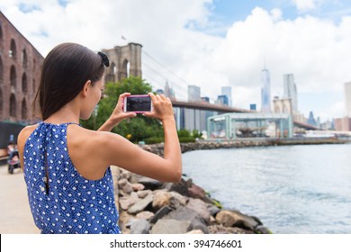 Tourist Taking Travel Picture With Phone Of Brooklyn Bridge And New York City Skyline During Summer Holidays. Unrecognizable Female Young Adult Enjoying USA Vacations In Blue Dress.