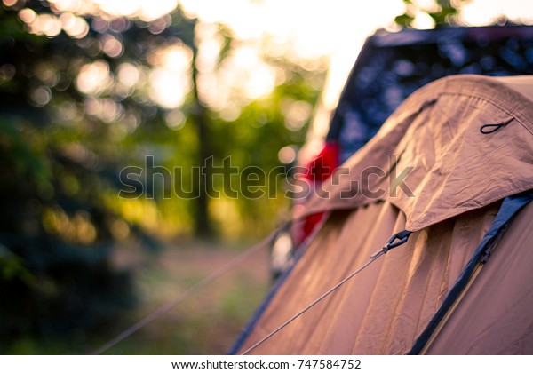 Tourist tent\
in forest camp among meadow and sunset. Travel tourist background\
with black car and mountain\
tent