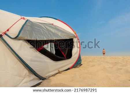Tourist tent on the seashore. A woman in a bathing suit is far away by the sea.
