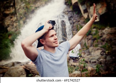 Tourist Traveler With An Action Camera Go On His Head In The Background Waterfall In Vietnam. Concept Of Extreme Holidays In The Mountains.