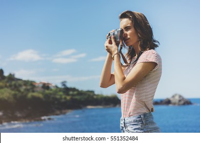 Tourist traveler photographer making pictures seascape on vintage photo camera on background yacht and boat piar, hipster girl enjoying peak nature holiday, mockup ocean waves view, blurred backdrop