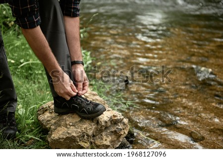 Tourist tying shoelaces placing his foot on a large stone by the stream, while trekking outdoors, shallow debth of field, selective focus. The concept of comfortable hiking shoes. Stock photo © 