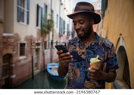 A tourist in Venice uses his smartphone while eating an ice cream, concept of technology on vacation