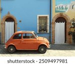 A tourist visiting Italy Romagna  Rimini Riccione Cattolica on hollyday summer looking a orange car 500 behing a colored facade of blue and yellow feeling armony and beauty