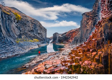 Tourist walking on the bottom of canyon with basalt columns. Unbelievable summer scene of Studlagil Canyon. Picturesque morning view of Iceland, Europe. Beauty of nature concept background.