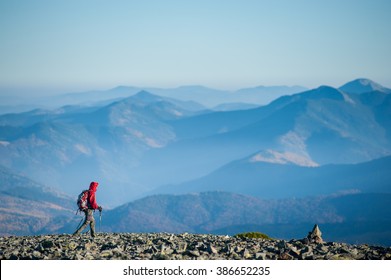 Tourist is walking on the rocky mountain on backpacking trip. Man is wearing red jacket and backpack on. Beautiful mountains on background. Eco tourism and healthy lifestyle concept. Copy space. - Shutterstock ID 386652235