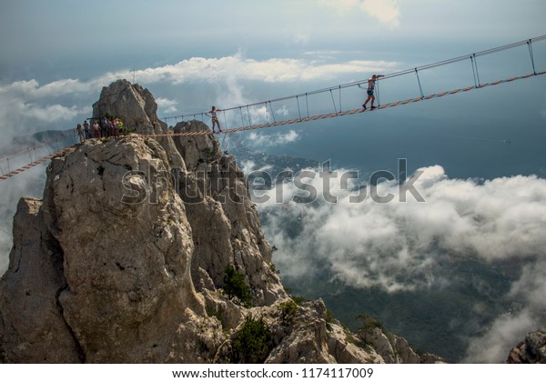 Tourist walks on a\
rope bridge on Mount Ai-Petri above abyss in Crimea. Man on a\
hanging bridge above the\
chasm.
