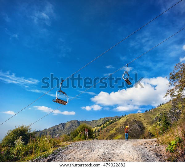 Tourist woman with\
backpack and yellow pointing to the cableway in the mountain ski\
resort at summertime
