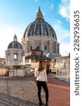 Tourist woman with detailed close up view on Michelangelos Dome of St Peter Basilica in Vatican City, Rome, Lazio, Europe, EU. Architectural masterpiece of Papal Basilica of Saint Peter on sunny day