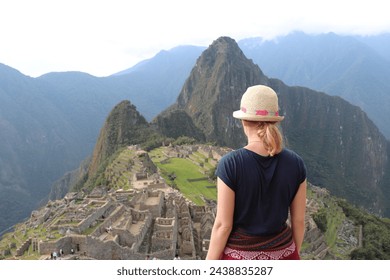 Tourist woman at historic old peruvian secret Inca ruin, ancient UNESCO landmark Machu Picchu with traditional stone wall houses and mountain landscape in sacred valley at Cusco, Peru, South America.