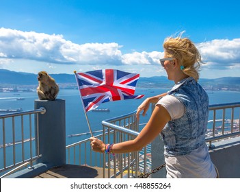Tourist woman holding an English flag observes one of the famous monkeys of Gibraltar from the top of Gibraltar Rock, in the Upper Rock Natural Reserve.