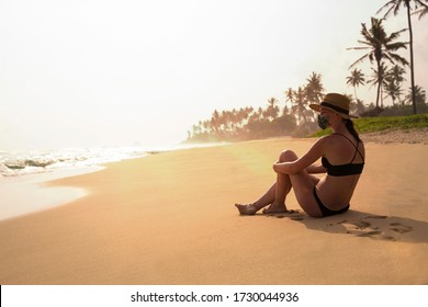 Tourist woman in medical face mask on beach. Young woman traveler with medical face mask sitting and relaxing on exotic beach surrounded by palm tree and sea.  - Powered by Shutterstock