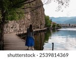 Tourist woman on morning walk on wooden platform The Bridge of Wishes extends into calm waters of Lake Ohrid, North Macedonia. Pier boardwalk with scenic views of lakeside, rolling hills and mountains