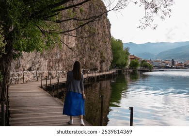 Tourist woman on morning walk on wooden platform The Bridge of Wishes extends into calm waters of Lake Ohrid, North Macedonia. Pier boardwalk with scenic views of lakeside, rolling hills and mountains - Powered by Shutterstock