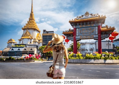A tourist woman on sightseeing tour stands in front of the Chinatown Gate at the famous Yaowarat Road, Bangkok, Thailand