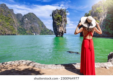 A tourist woman in a red dress looks at the famous sightseeing spot James Bond island at Phang Nga Bay, Phuket, Thailand