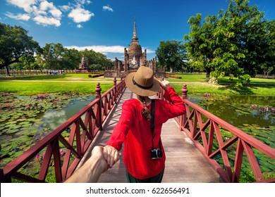 Tourist Woman in red shirt holding her husband by hand and going to ancient stupa in Sukhohai Historical Park, Thailand