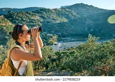 Tourist woman resting in olive grove, looking through binoculars at the mountains view. Traveling or exercising outdoors. Active people, hiking, healthy lifestyle and harmony concept.Unity with nature - Powered by Shutterstock